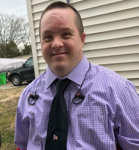 Man with down syndrome smiling and wearing a blue checkered button down with headphones around his neck