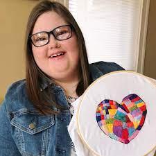 Woman with Down syndrome smiles while holding a patterned heart piece of art