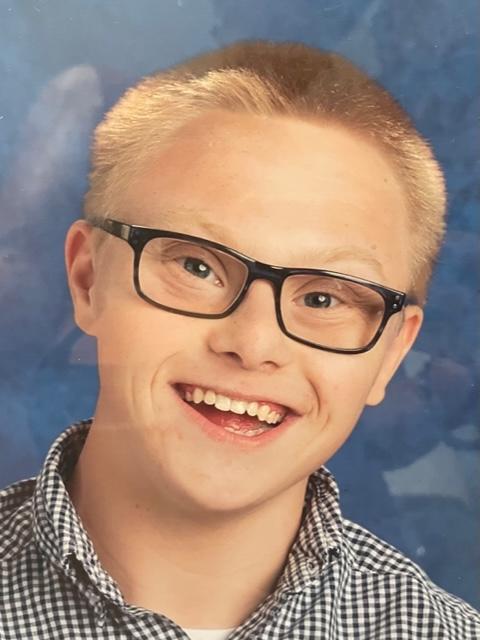 blonde haired boy with Down syndrome smiles at the camera for his headshot
