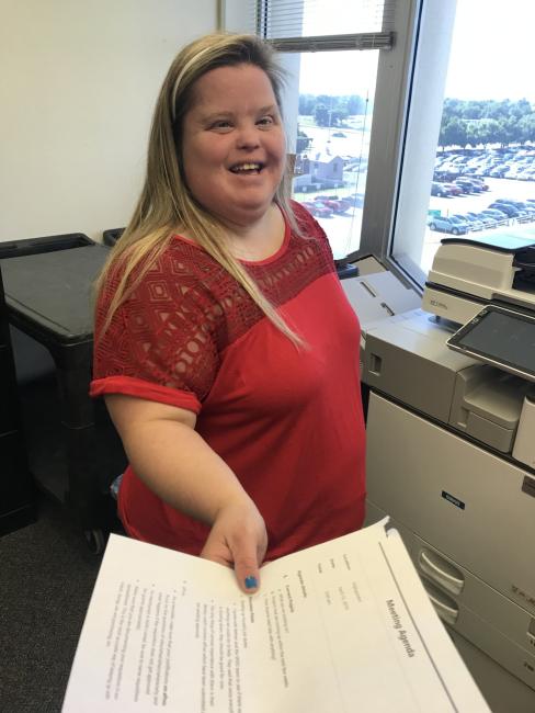 Heather, a blonde woman with Down syndrome, hands someone a document in the office.