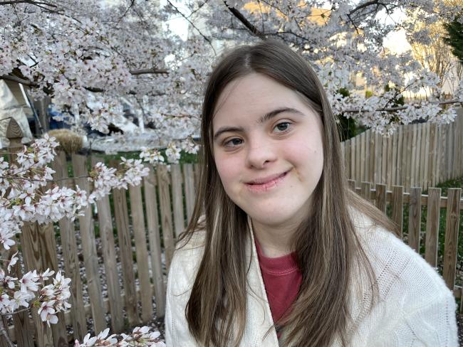 Photo of woman with Down syndrome standing in front of a flowering tree