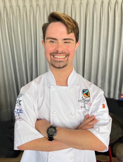 A Puerto Rican man with Down syndrome is wearing a white chef's coat 