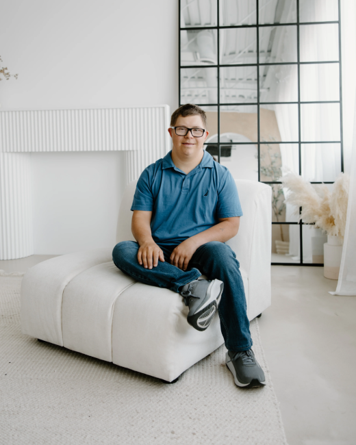A man with Down syndrome sits on a white sofa in a white and airy studio room