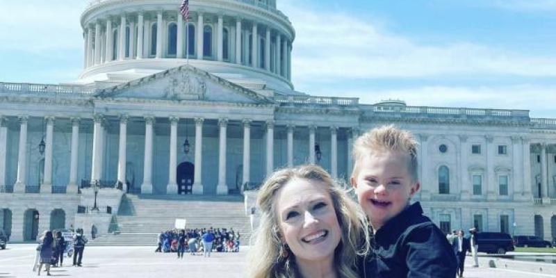 woman holds her son with down syndrome as they post smiling in front of the US Capitol