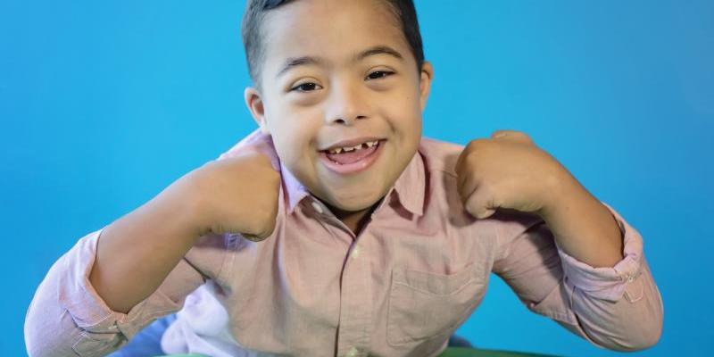 Young boy with brown hair and Down syndrome smiles at the camera