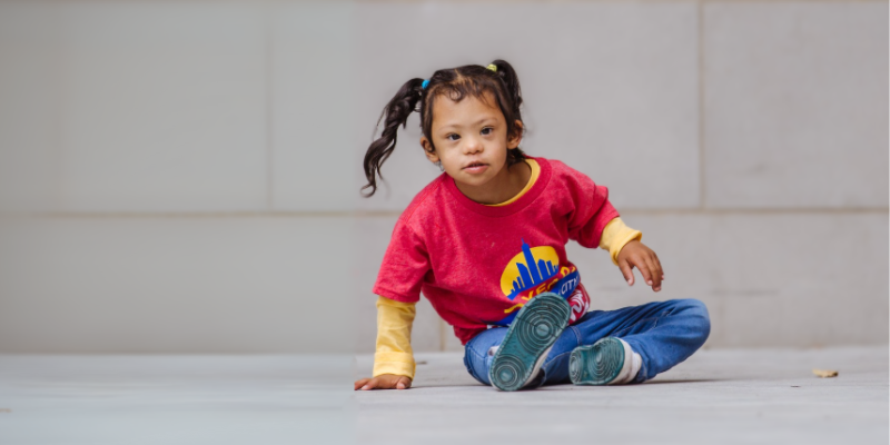 Young girl with Down syndrome and pigtails sits on stage