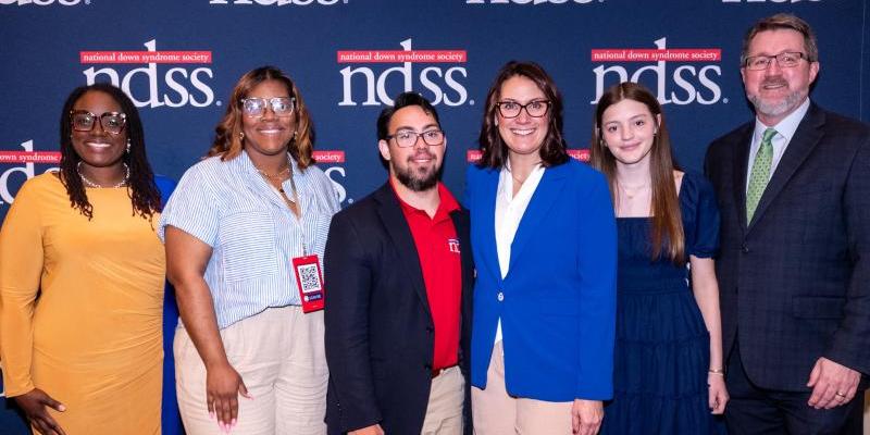 A group of advocates stands in front of an NDSS backdrop